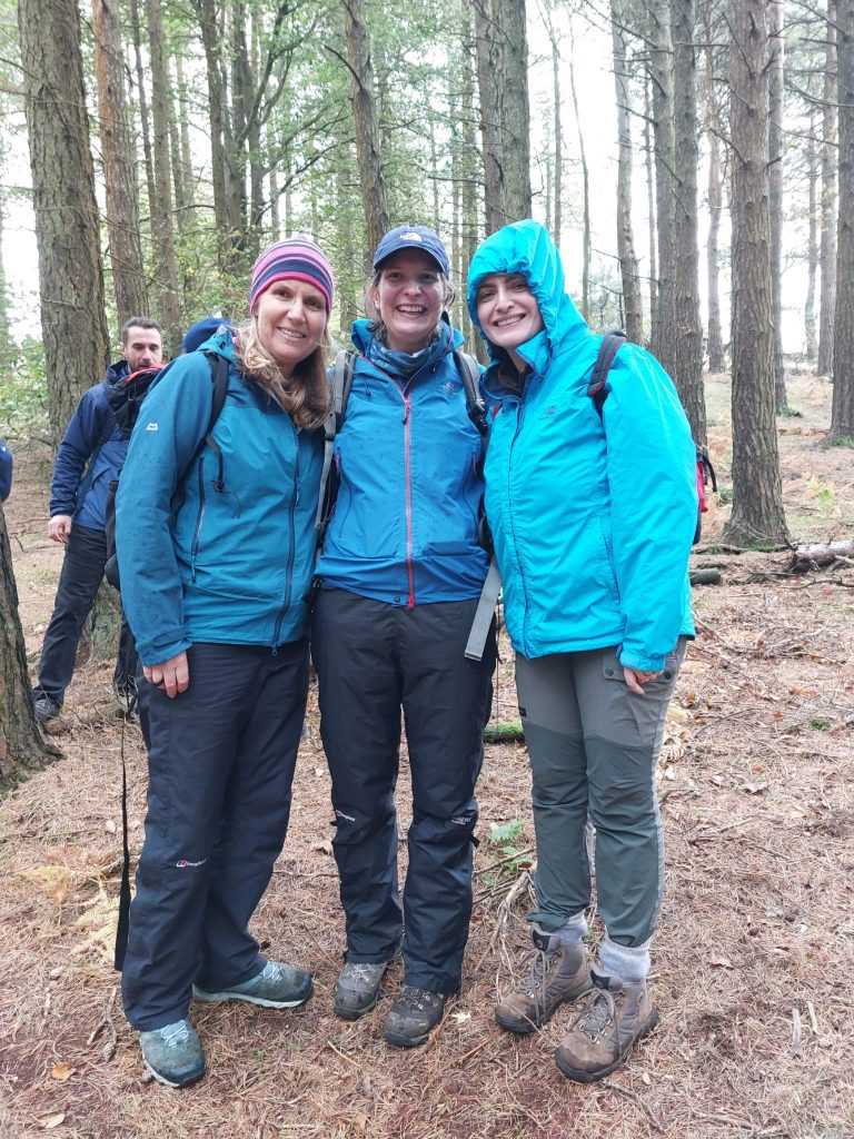 Three walkers on a Green Therapy event. They are wearing waterproof jackets, walking trousers and boots. They are standing in woodland, smiling at the camera.